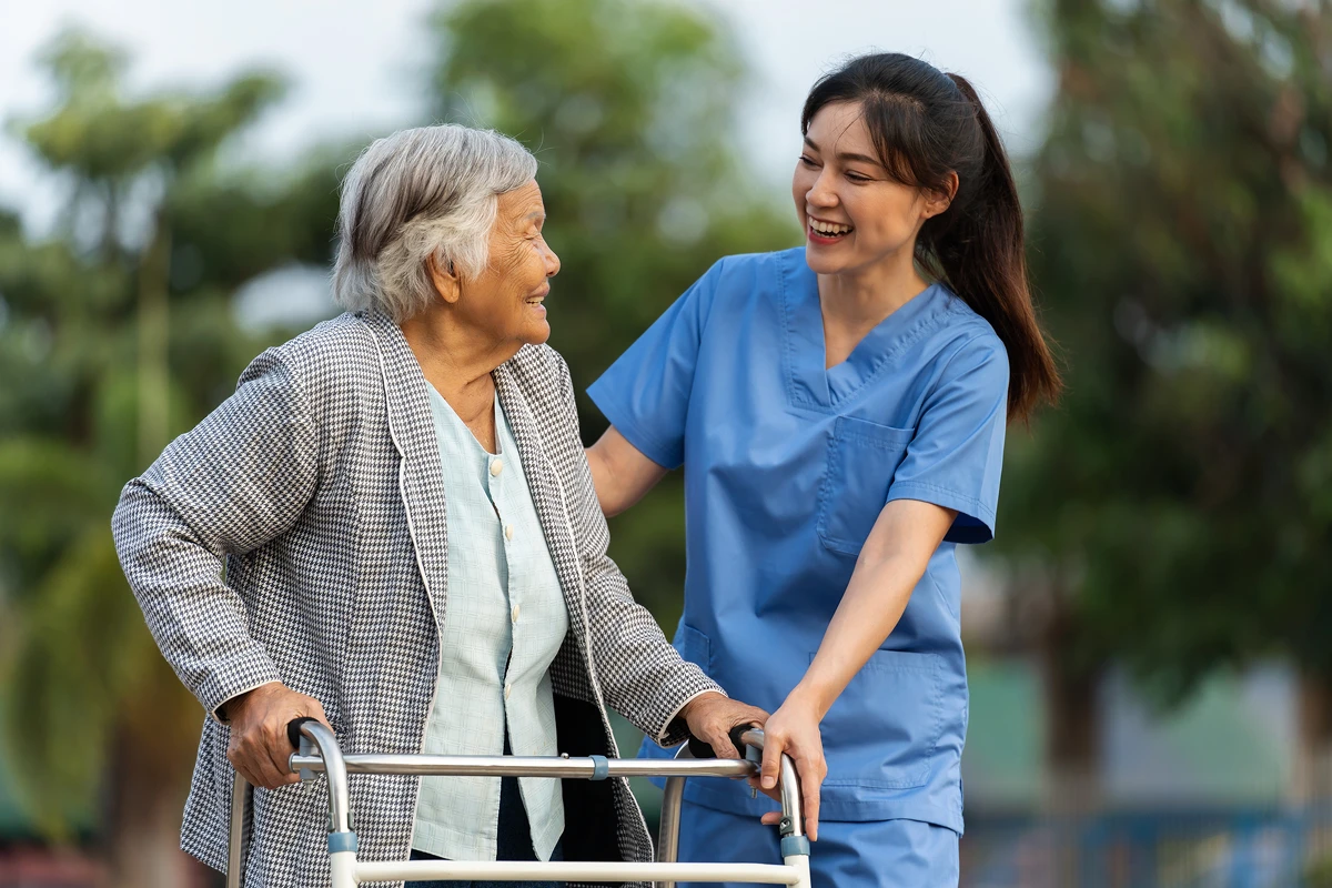 Caregiver assisting elderly woman with walker.