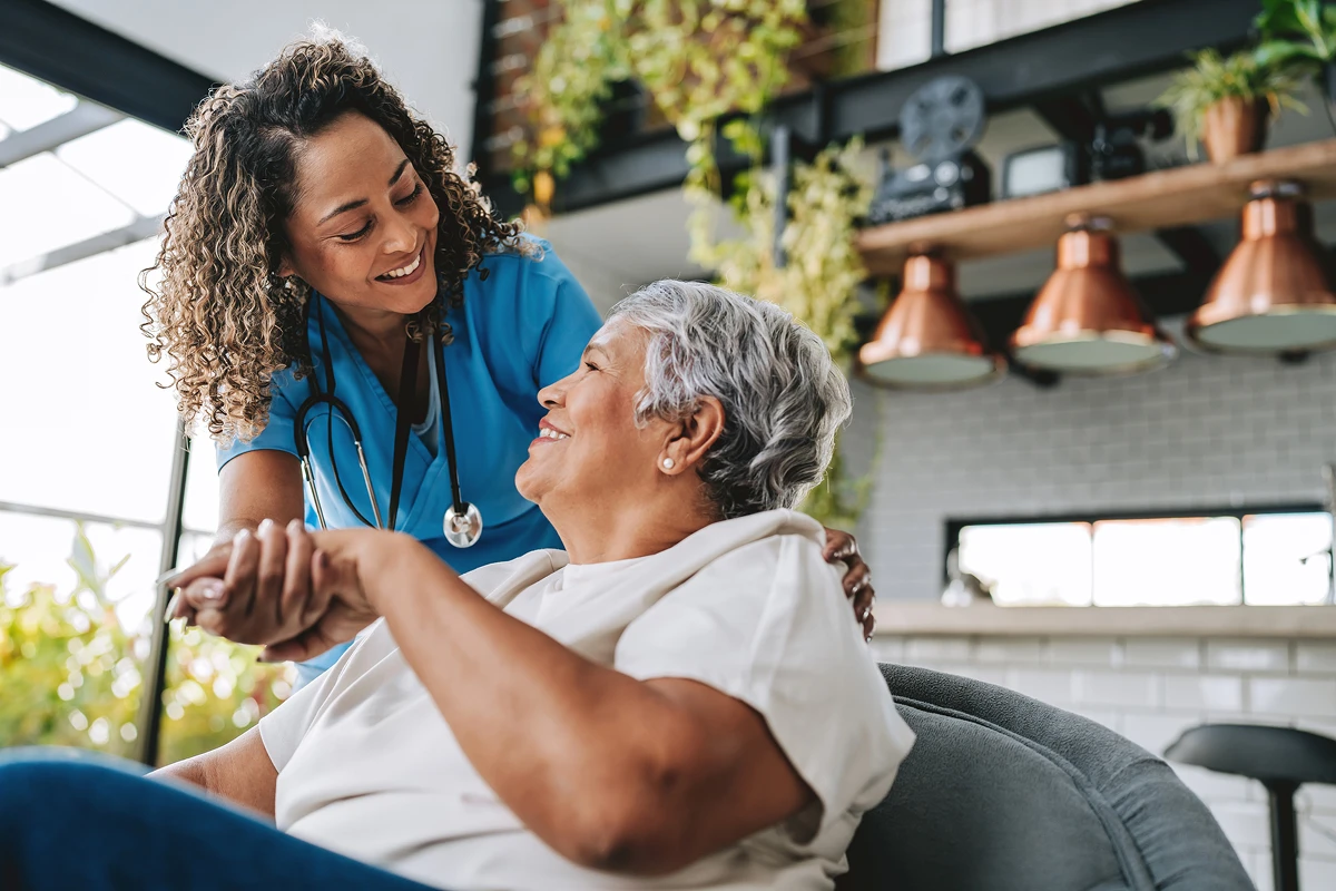 Nurse assisting elderly woman at home smiling.